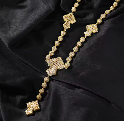A silver-colored rosary bead chain necklace with baguette cut cubic zirconia stones and cross-shaped pendants, displayed on a black background.