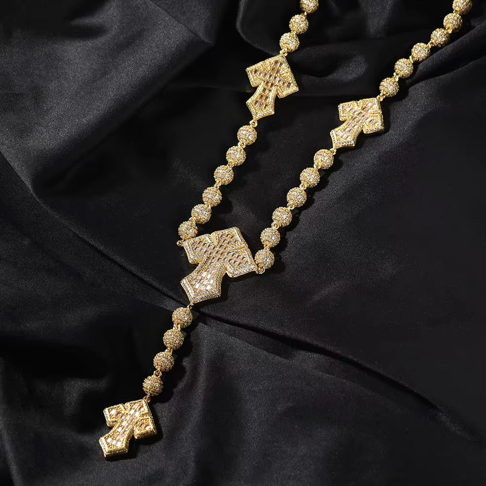 A silver-colored rosary bead chain necklace with baguette cut cubic zirconia stones and cross-shaped pendants, displayed on a black background.